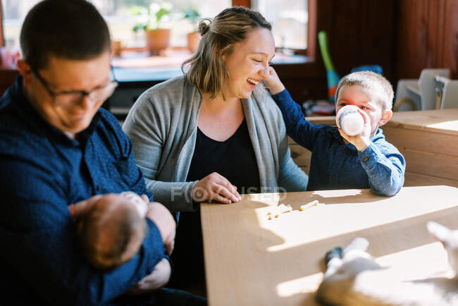 Молодая семья сидит за обеденным столом с новорожденным и малышом — стоковое фото