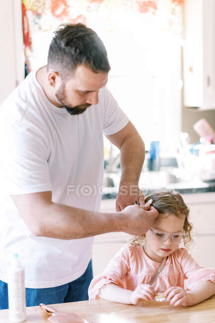 Un padre y su hija arreglándose el pelo para el día escolar - foto de stock