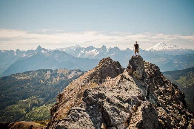 Hiker stands on summit of mountain with scenic view behind. — Stock Photo