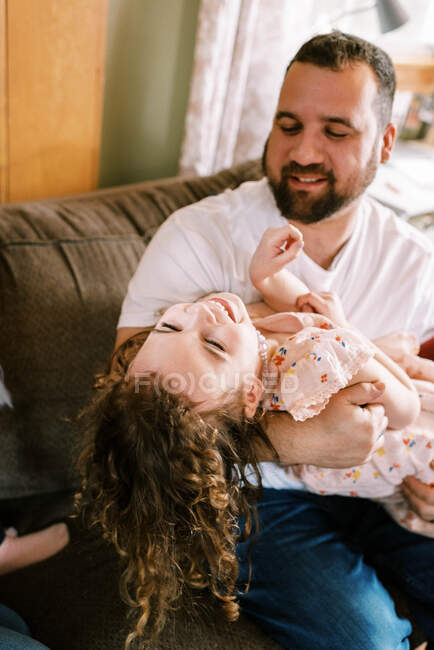 Joven padre e hija jugando juntos en la sala de estar y riendo - foto de stock