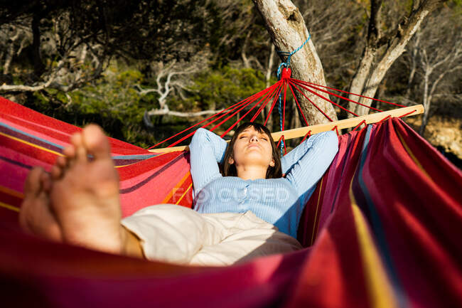 Young woman sunbathing in hammock hanging in pine trees — Stock Photo