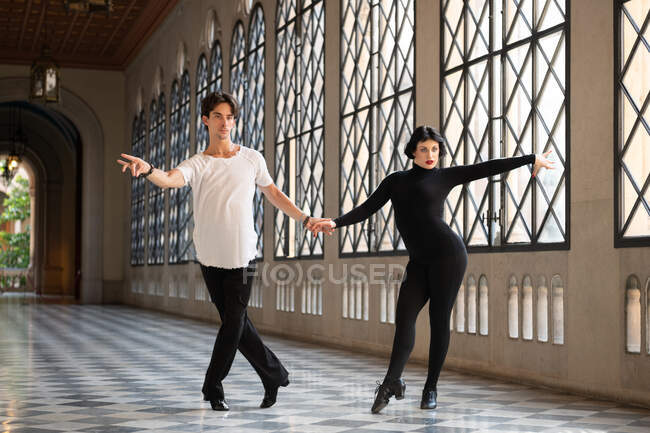 Hombre y mujer tomados de la mano y practicando pasos durante el ensayo de danza latina - foto de stock