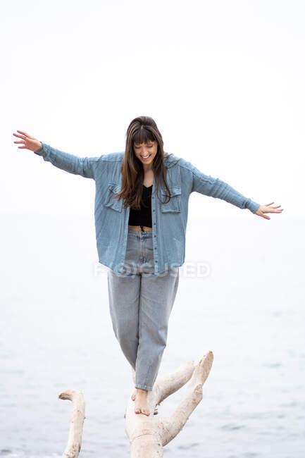 Mujer joven de pie sobre tronco de madera blanca con el mar en el fondo - foto de stock