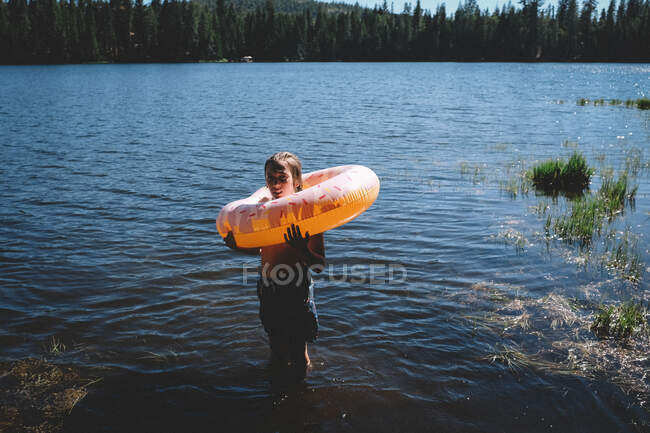 Tween stand on a lakeshore with inflatable donut around his neck — Stock Photo