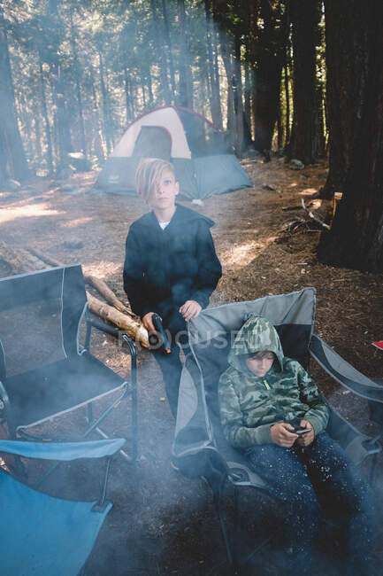 Zwei Jungen am Lagerfeuer im Wald mit Telefon und BB Gun. — Stockfoto