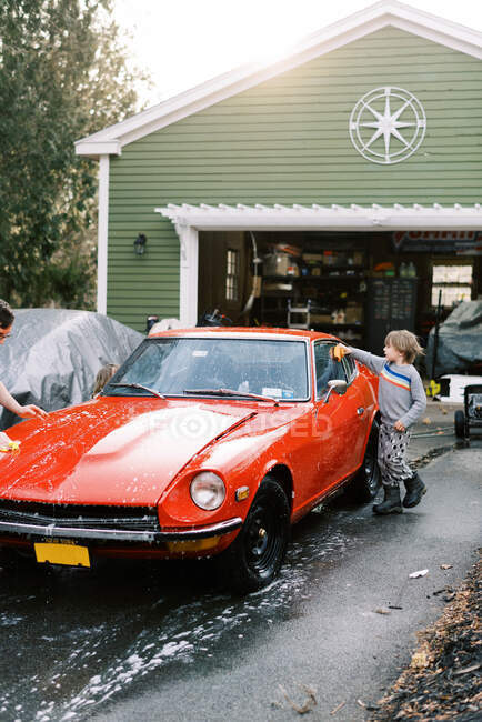 Ragazzino in maglione che lava una macchina classica fuori in primavera con papà — Foto stock