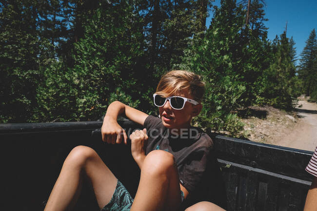 Boy in White Sunglasses Rides in the Back of truck on a dirt road — Stock Photo