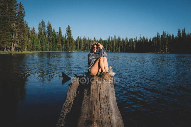Blonde Frau posiert bei Sonnenuntergang auf einem Baumstamm über Wasser. — Stockfoto