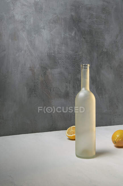 Stillleben mit leerer Flasche und Zitronen auf grauweißem Hintergrund — Stockfoto