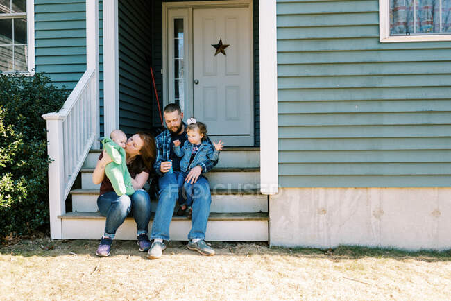 Eine glückliche Familie sitzt mit ihren Töchtern vor der Haustür — Stockfoto