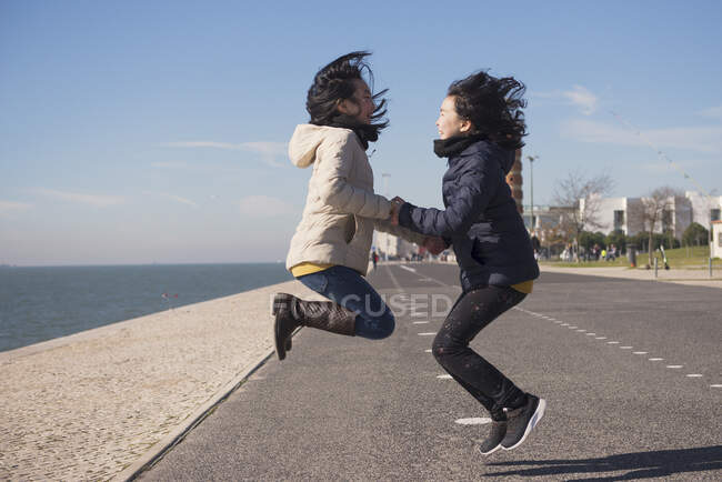 Meninas alegres estão pulando nas margens do rio na cidade. — Fotografia de Stock