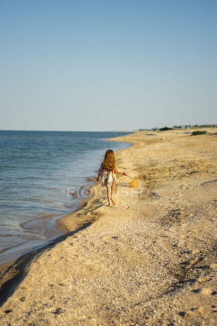 Uma menina caminha ao longo do mar na praia ao pôr do sol — Fotografia de Stock