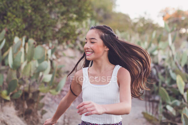 Chica de raza mixta caminando en un sendero de cactus con su pelo largo volando. - foto de stock