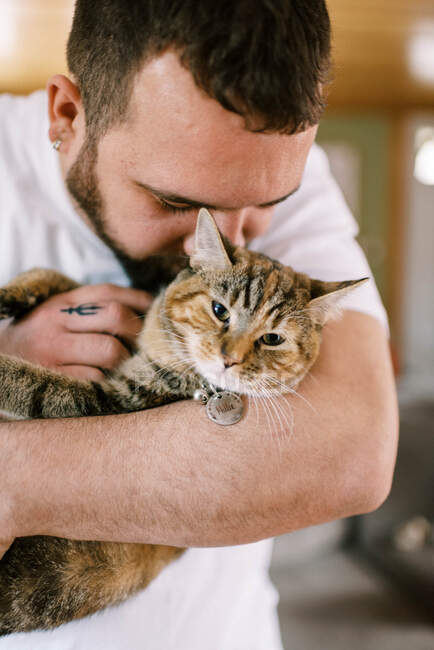 Мужчина держит свою кошку на руках и обнимается с ней с любовью. — стоковое фото
