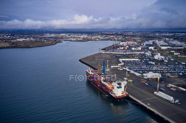 Drone vista del moderno puerto de carga con barcaza de envío y edificios de almacenamiento con grúas bajo nubes oscuras - foto de stock