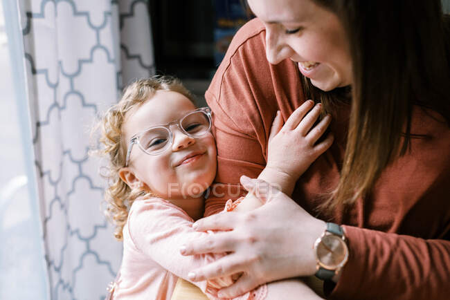 Ein Kleinkind mit Brille umarmt seine Mutter am Küchentisch — Stockfoto
