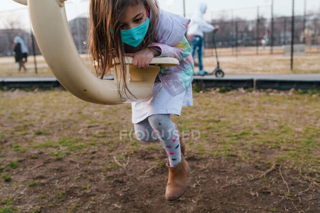 Junges Mädchen mit Gesichtsmaske klettert auf Säge auf Spielplatz — Stockfoto