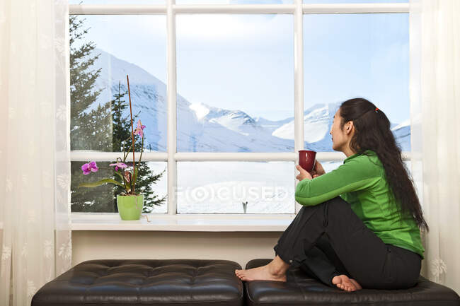 Mujer mirando por la ventana a la casa de vacaciones islandesa - foto de stock