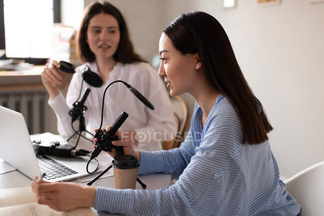 Asian blogger talking into microphone during podcast with friend in studio — Stock Photo