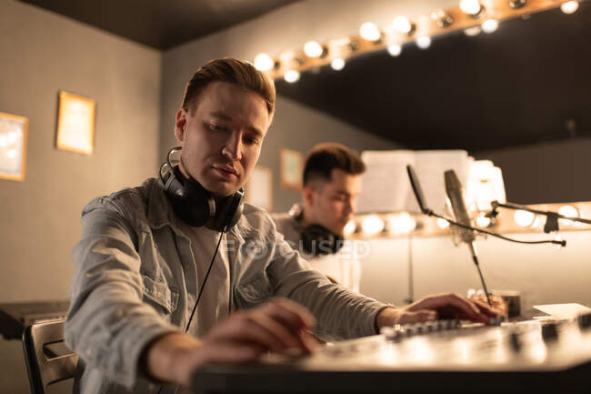 Homme professionnel utilisant une carte son pour enregistrer une chanson près d'un collègue dans un studio moderne — Photo de stock