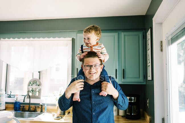 Усміхнений батько тримає сина на плечах на кухні — стокове фото