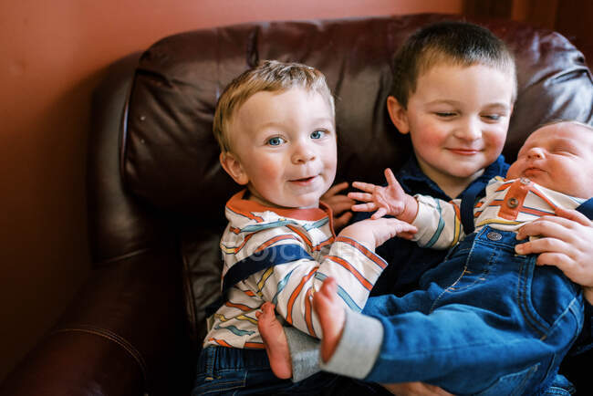 Little toddler sitting next to his siblings on an arm chair smiling — Stock Photo