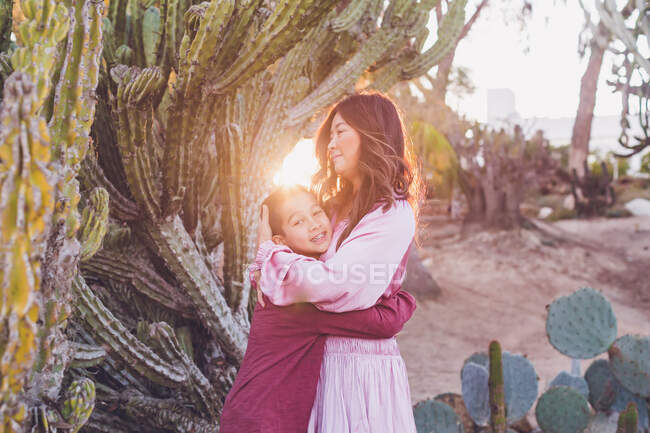 Мати обіймає сина перед великим кактусом із заднім світлим сонцем . — стокове фото