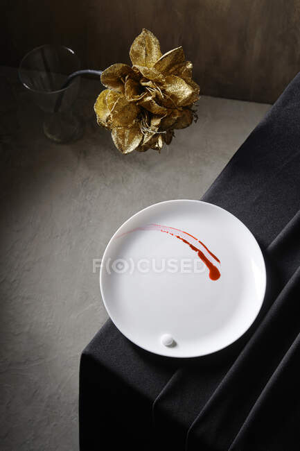 Натюрморт с белой тарелкой на черном столе и желтым цветком — стоковое фото