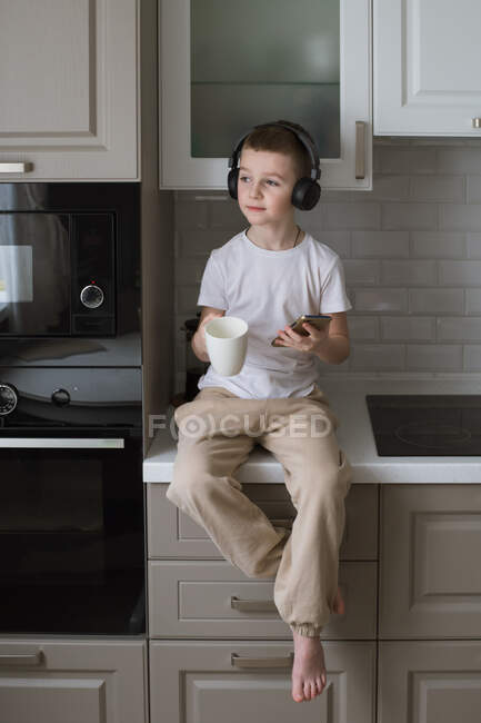 Niño escuchando música con auriculares mientras usa el teléfono - foto de stock