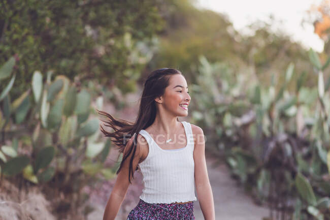 Menina de raça mista andando em uma trilha de cacto com seu cabelo longo voando. — Fotografia de Stock