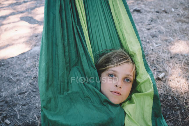 Блондинка Одягнена дитина дивиться з зеленого гамака — стокове фото