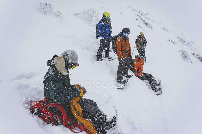 Personnes avec des planches à neige sur la pente de la montagne enneigée pendant les chutes de neige — Photo de stock