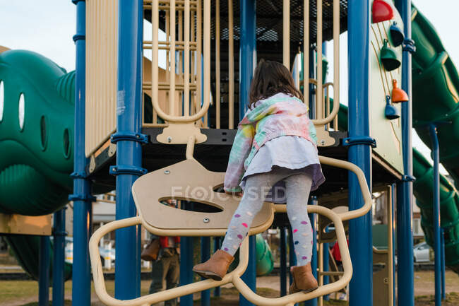 Girl climbing playground equipment wearing dress and tights — Stock Photo