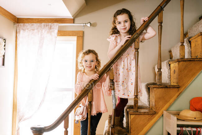 Grande y pequeña hermana de pie en la escalera de madera sonriendo juntos - foto de stock
