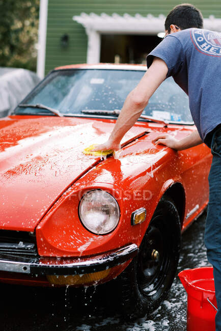 Homme millénaire laver une voiture rouge classique à la main dans son allée — Photo de stock