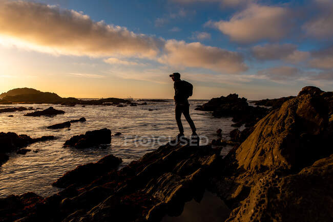 Figura silueta de pie en la orilla con dramática puesta de sol en el cielo - foto de stock