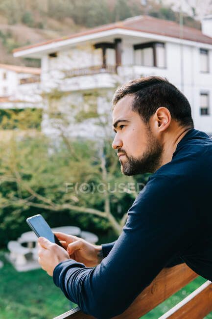Hombre con teléfono inteligente mirando hacia el balcón de su casa - foto de stock