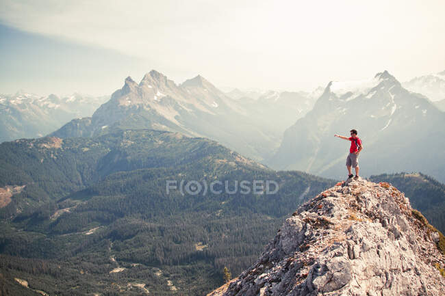 Hiker pointing across valley from rocky mountain summit — Stock Photo