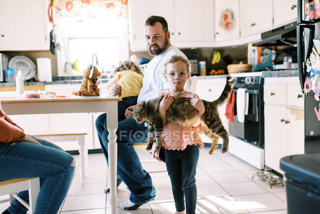 Маленькая девочка держит свою милую кошку на руках на кухне. — стоковое фото