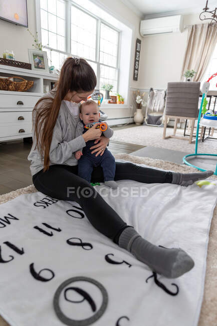 Liebevolle Mutter sitzt auf dem Boden und hält ihren glücklichen kleinen Jungen. — Stockfoto