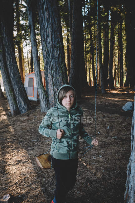 Tween in Camo Hoodie stands with swing at campsite. — Stock Photo