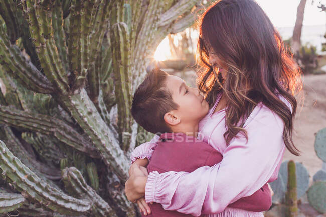 Mãe abraçando filho, ambos olhando um para o outro com sol luz nas costas. — Fotografia de Stock