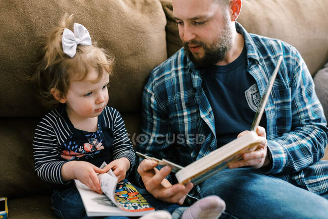 Молодий батько спілкується зі своєю донькою і читає разом — стокове фото