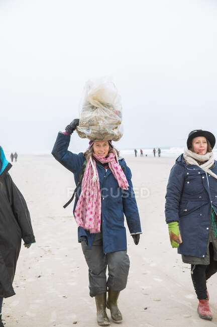Reif frau balancing müllsack auf kopf nach cleanup im strand — Stockfoto
