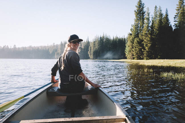 Улыбающаяся женщина оглядывается через плечо, катаясь на каноэ по озеру — стоковое фото