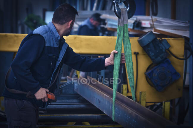 Man putting steel beam on cutting machine with crane — Stock Photo