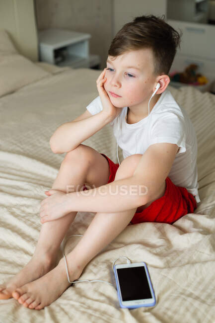 Мальчик слушает музыку с наушниками на кровати — стоковое фото