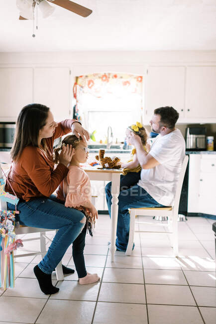 Deux parents coiffant leurs filles jumelles cheveux ensemble dans la cuisine — Photo de stock