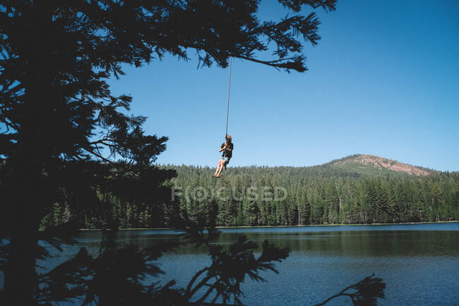 Ragazzo oscilla fuori alto sopra l'acqua su una corda swing — Foto stock
