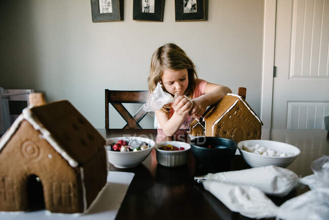 Menina decorando casas de gengibre com cobertura e doces — Fotografia de Stock